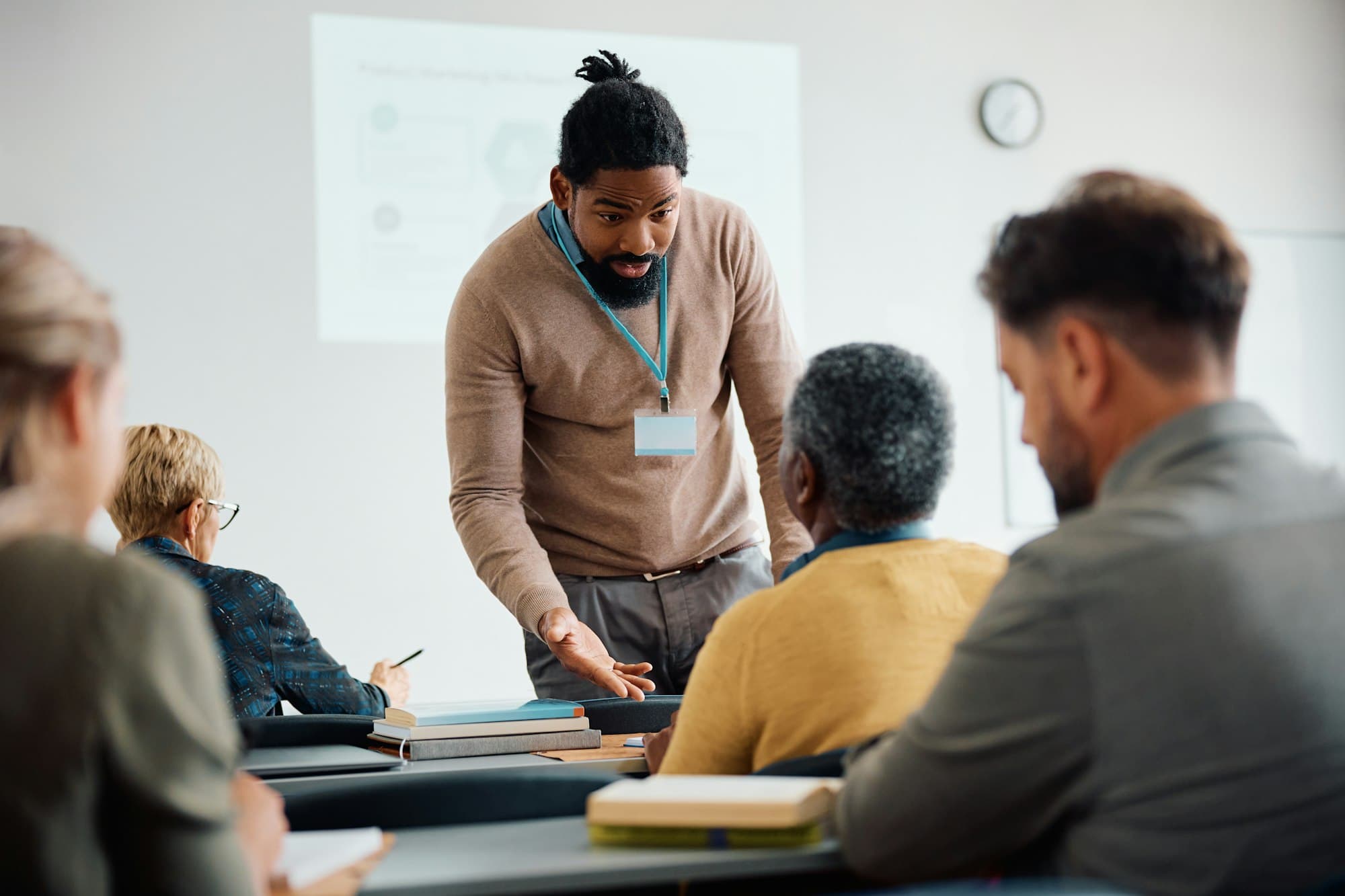 Black teacher talking to senior man during adult education training class in lecture hall.